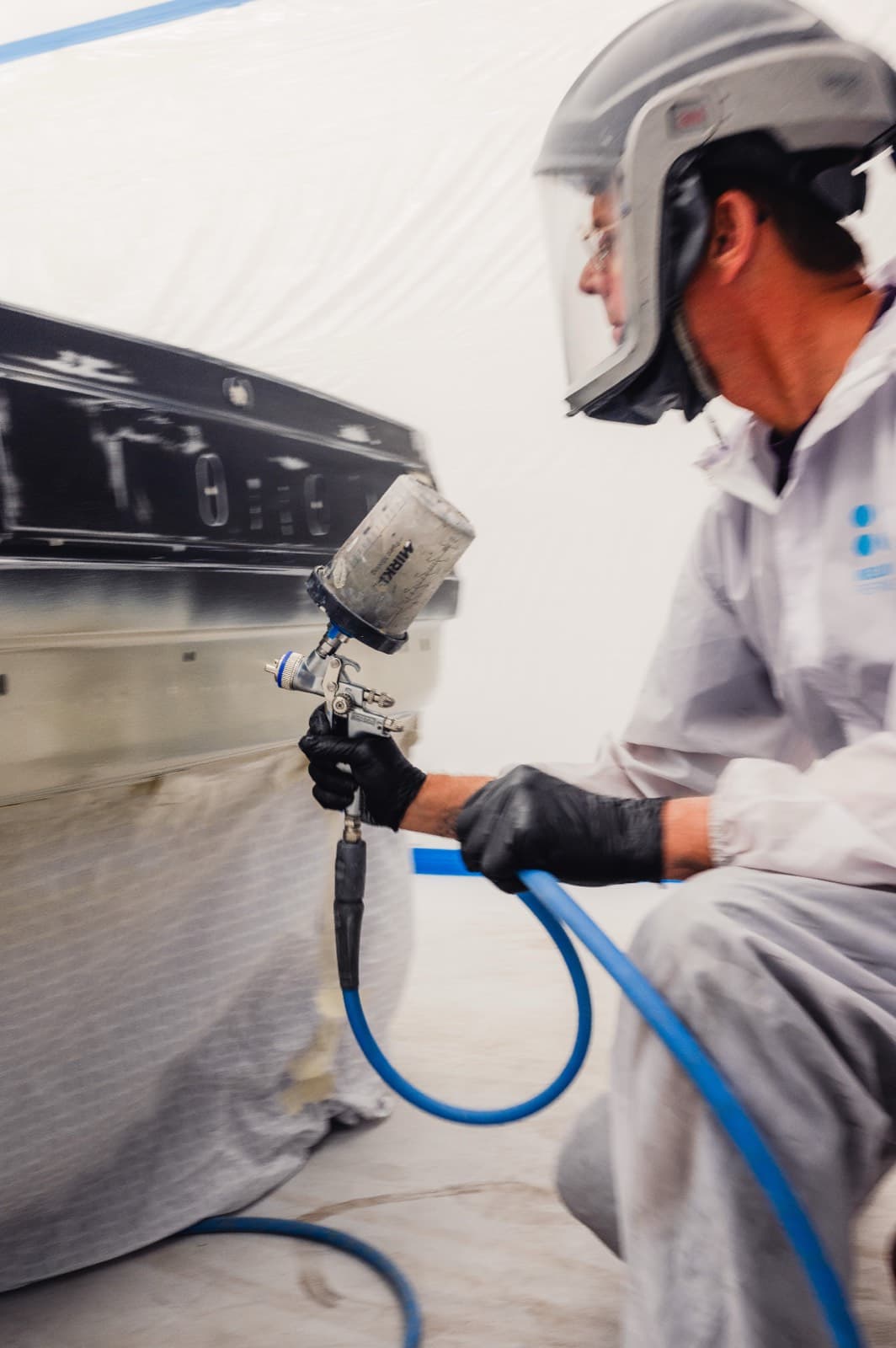 Technician in protective suit applying paint with spray gun in paint booth