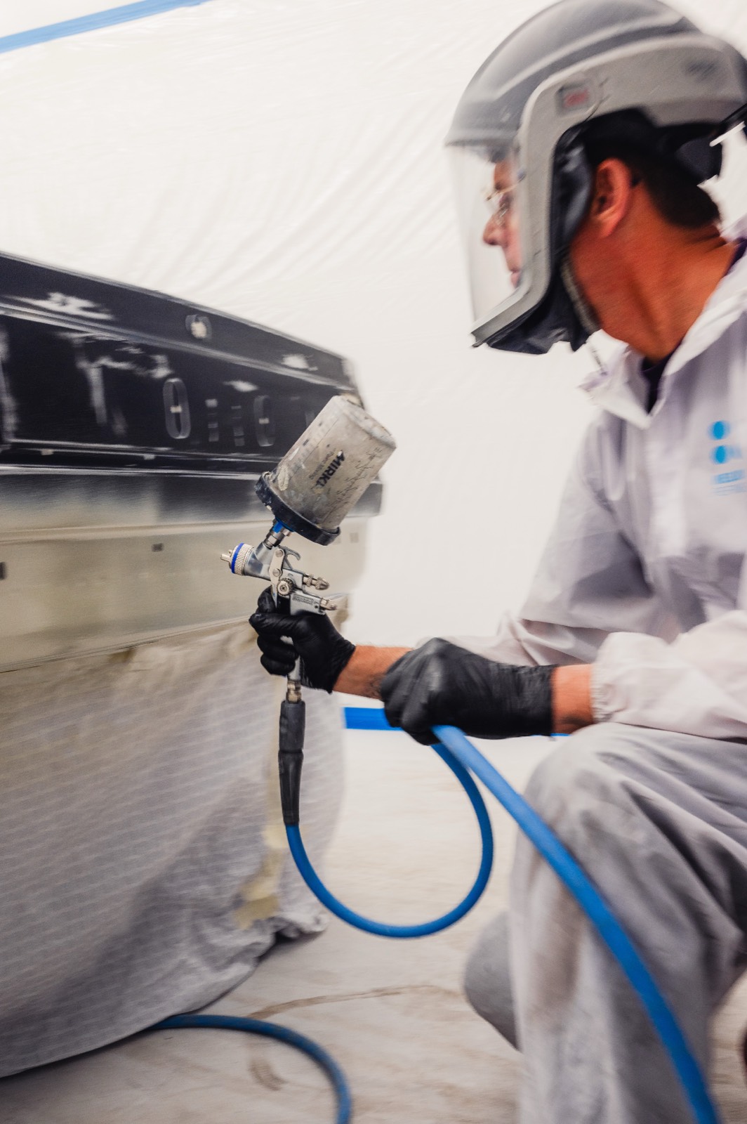Technician in protective suit applying paint with spray gun in paint booth